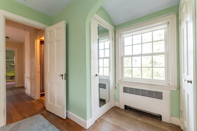 doorway to outside featuring radiator, baseboards, light wood-type flooring, and arched walkways