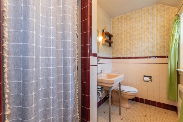 full bathroom featuring tile patterned flooring, wainscoting, toilet, tile walls, and wallpapered walls