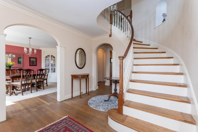 entryway with wood finished floors, baseboards, stairway, arched walkways, and a notable chandelier