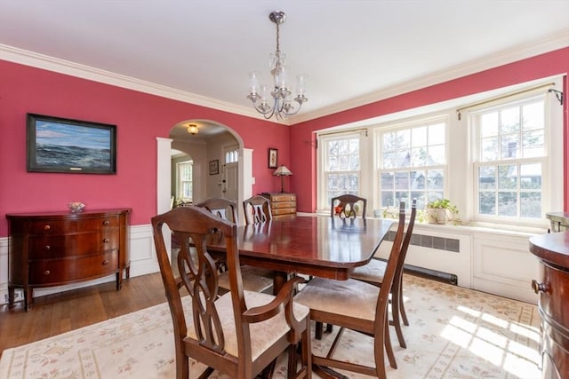 dining room featuring arched walkways, a chandelier, a wealth of natural light, and radiator heating unit