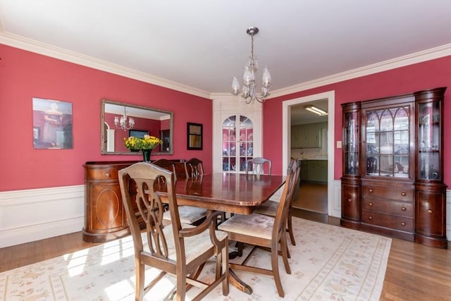 dining room featuring a wainscoted wall, ornamental molding, wood finished floors, and a chandelier