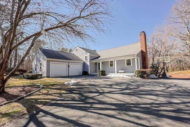 view of front of home featuring driveway, a porch, a chimney, and an attached garage