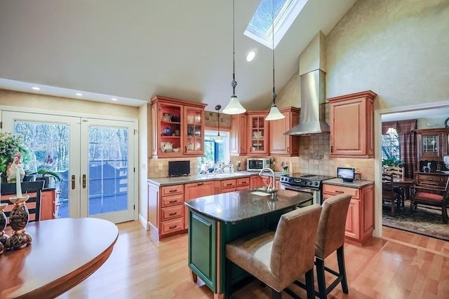 kitchen featuring french doors, appliances with stainless steel finishes, high vaulted ceiling, light wood-type flooring, and wall chimney exhaust hood