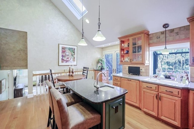 kitchen featuring a skylight, light wood finished floors, glass insert cabinets, a sink, and high vaulted ceiling