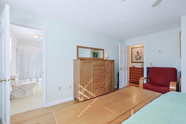 bedroom featuring ensuite bath, wood finished floors, a ceiling fan, and baseboards