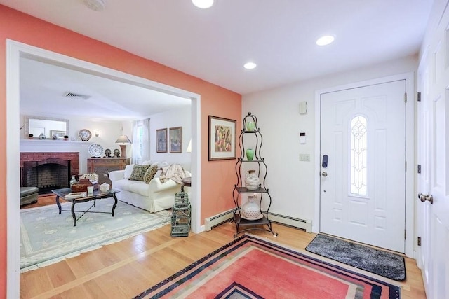 foyer entrance with light wood finished floors, recessed lighting, visible vents, baseboard heating, and a brick fireplace