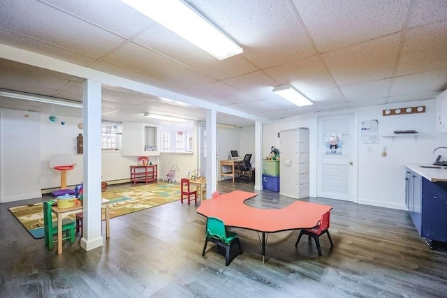 game room with dark wood-style floors, a drop ceiling, a sink, and baseboards