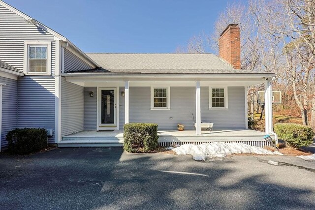 doorway to property with a porch, a chimney, and a shingled roof