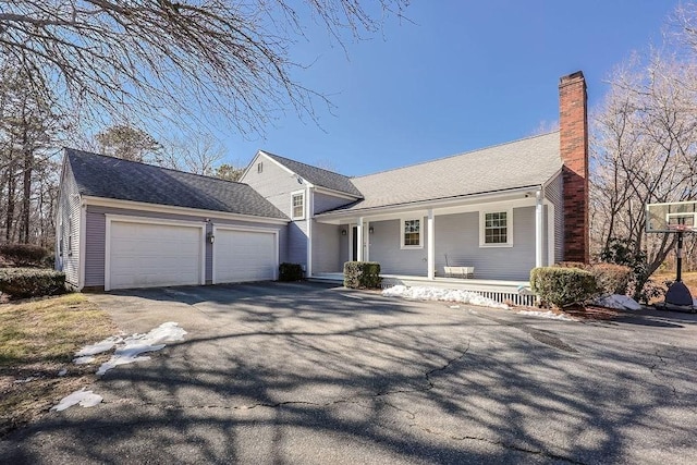 view of front facade with a garage, covered porch, driveway, and a chimney