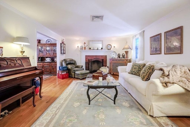 living room with light wood finished floors, a brick fireplace, visible vents, and crown molding