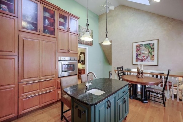 kitchen with pendant lighting, stainless steel oven, a sink, dark stone countertops, and light wood-type flooring