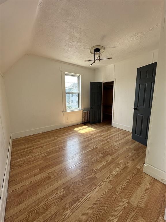 99 Allston St, Lawrence, MA 01841 - unfurnished bedroom featuring radiator heating unit, a textured ceiling, light wood-type flooring, baseboards, and lofted ceiling