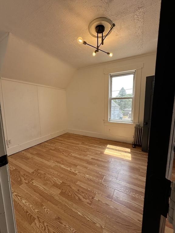 99 Allston St, Lawrence, MA 01841 - bonus room featuring radiator, a textured ceiling, light wood-style flooring, vaulted ceiling, and a chandelier
