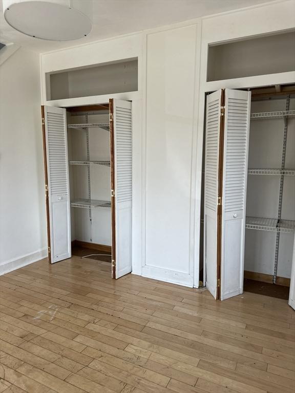 99 Allston St, Lawrence, MA 01841 - unfurnished bedroom featuring light wood-style flooring, baseboards, and two closets