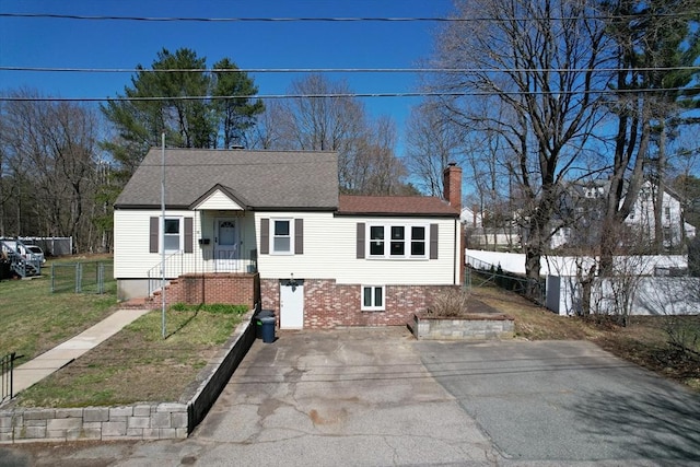 view of front facade featuring a front yard, a shingled roof, a chimney, fence, and brick siding