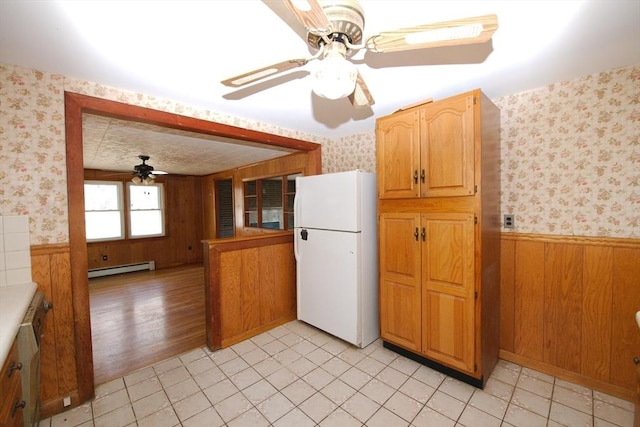 kitchen featuring a baseboard radiator, freestanding refrigerator, a ceiling fan, wallpapered walls, and a wainscoted wall
