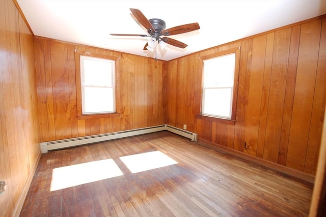 empty room featuring wooden walls, baseboard heating, a ceiling fan, and wood finished floors