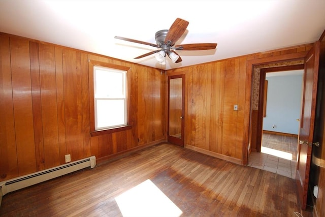unfurnished room with baseboard heating, wood finished floors, ceiling fan, and baseboards