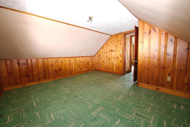 additional living space featuring wooden walls, baseboards, and vaulted ceiling