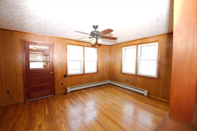 interior space with wood walls, ceiling fan, a baseboard heating unit, and wood finished floors