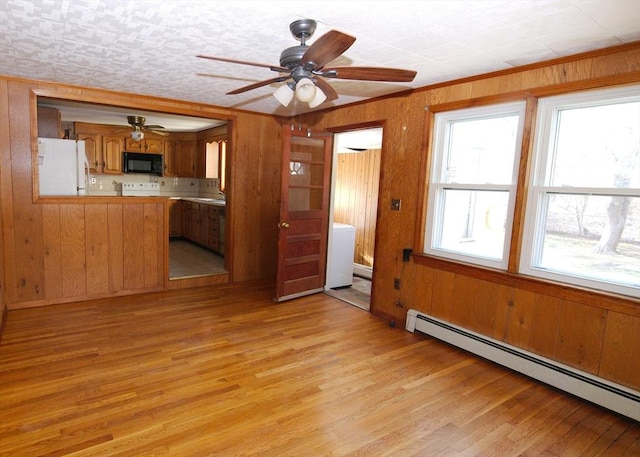 kitchen with freestanding refrigerator, black microwave, brown cabinetry, a ceiling fan, and a baseboard radiator