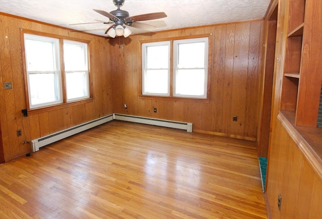 unfurnished room with light wood-style flooring, wood walls, ceiling fan, and a baseboard radiator