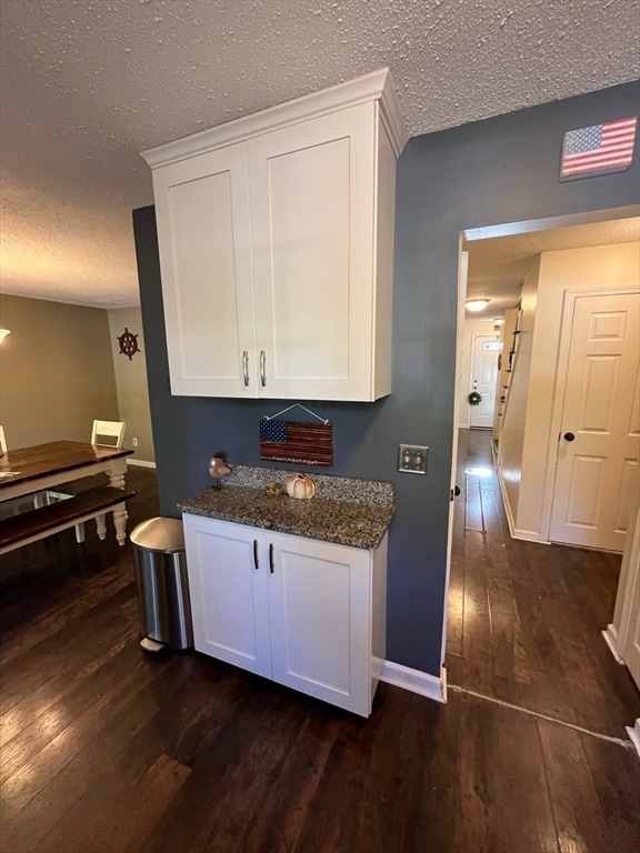 bar featuring white cabinets, a textured ceiling, dark hardwood / wood-style floors, and dark stone counters