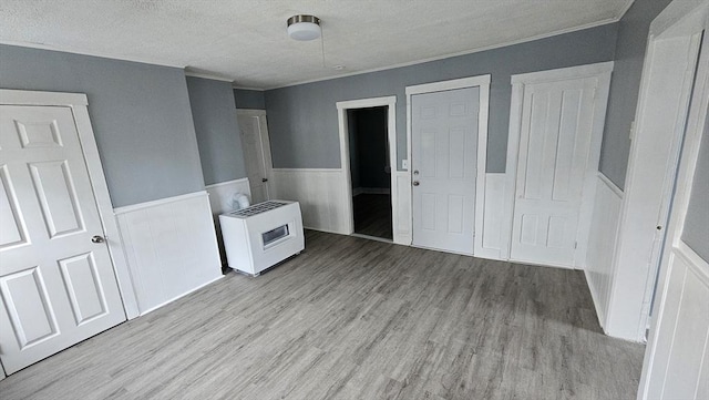 unfurnished bedroom featuring a textured ceiling, light wood-type flooring, heating unit, and crown molding