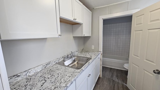 kitchen with dark hardwood / wood-style flooring, white cabinetry, sink, and light stone counters