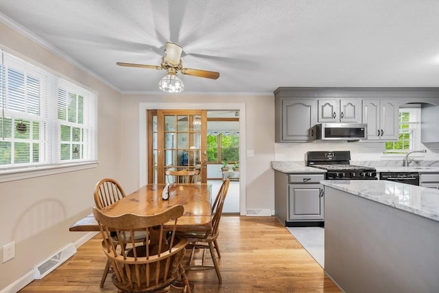 kitchen featuring black gas stove, gray cabinetry, stainless steel microwave, healthy amount of natural light, and crown molding