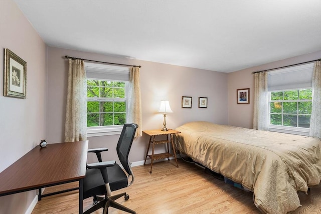 bedroom featuring multiple windows, light wood-style floors, baseboards, and a desk