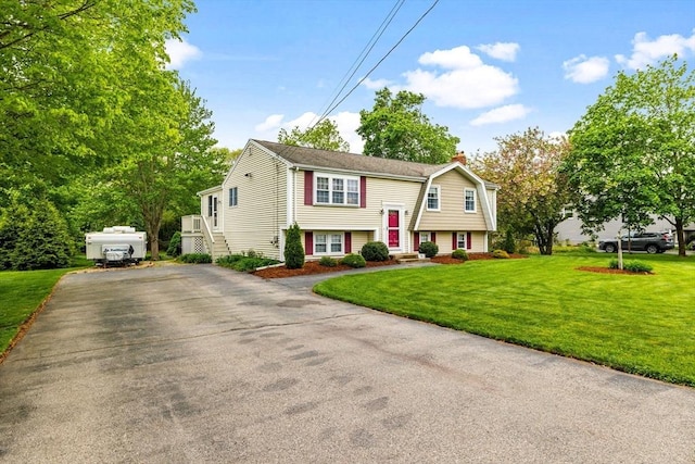 split foyer home featuring a chimney, asphalt driveway, and a front yard