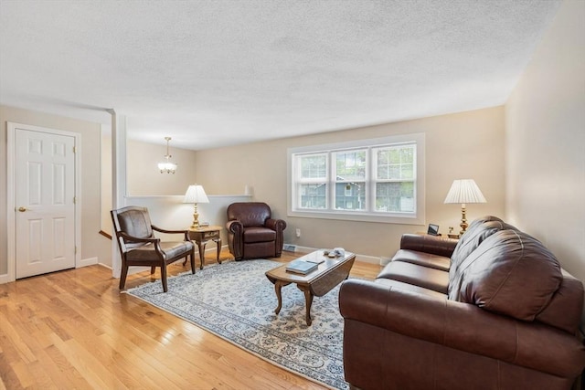 living area featuring light wood finished floors, a textured ceiling, a chandelier, and baseboards