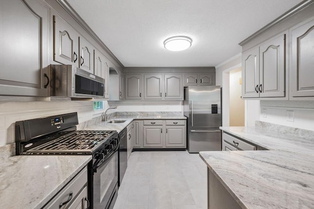 kitchen featuring appliances with stainless steel finishes, gray cabinetry, a sink, light stone counters, and a textured ceiling