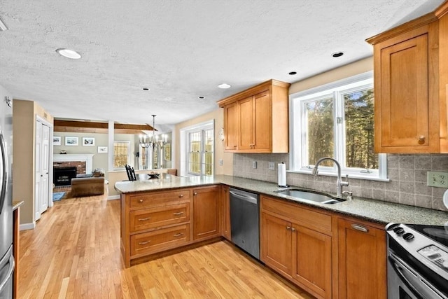 kitchen featuring appliances with stainless steel finishes, pendant lighting, sink, kitchen peninsula, and a brick fireplace