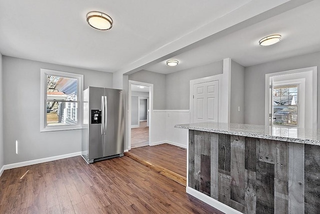 kitchen featuring stainless steel fridge, plenty of natural light, dark wood-type flooring, and light stone counters