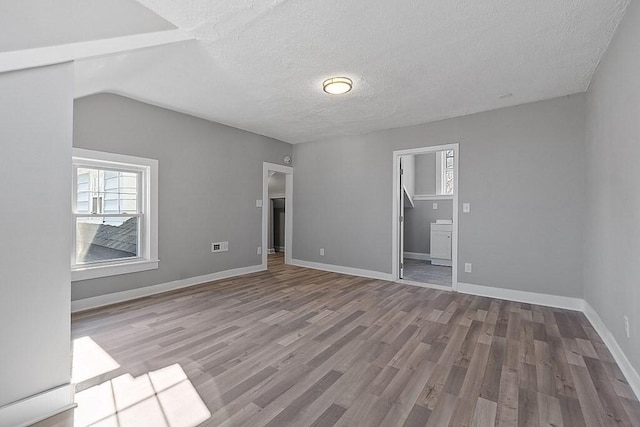 unfurnished bedroom featuring wood finished floors, a textured ceiling, baseboards, ensuite bath, and lofted ceiling
