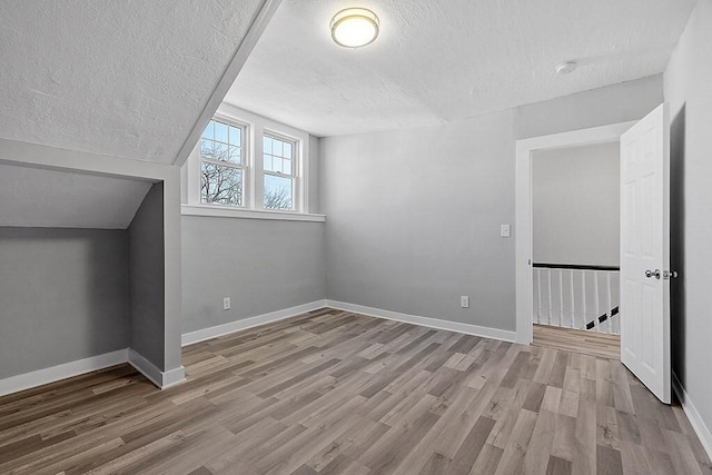 additional living space with a textured ceiling, wood finished floors, and baseboards