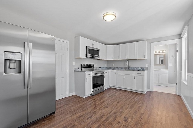 kitchen with appliances with stainless steel finishes, light stone countertops, white cabinets, and dark wood-style flooring