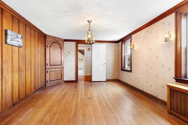 spare room with baseboards, light wood finished floors, wallpapered walls, radiator heating unit, and a notable chandelier