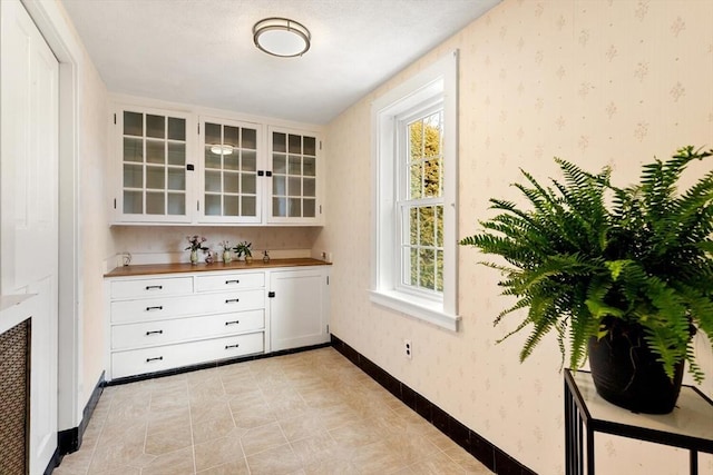 bar featuring wallpapered walls, light tile patterned floors, and baseboards