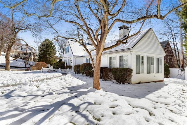 view of snow covered exterior with a chimney and fence