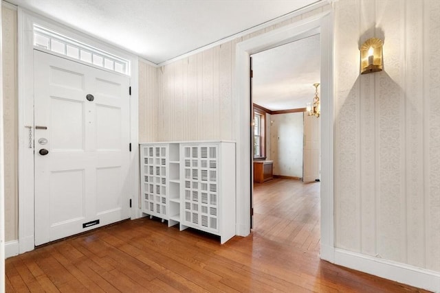 foyer entrance with wallpapered walls, hardwood / wood-style flooring, and a chandelier