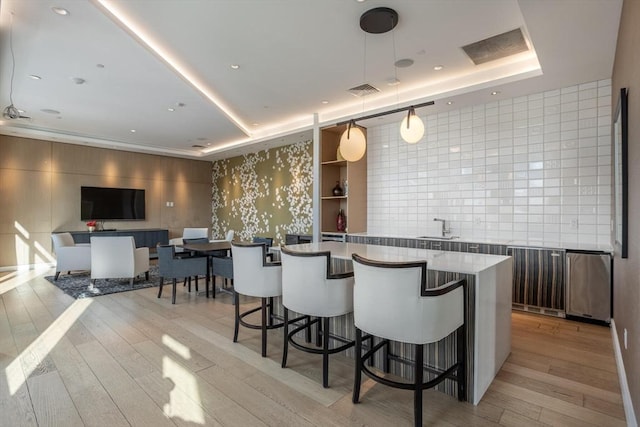 kitchen with decorative light fixtures, a tray ceiling, a kitchen breakfast bar, a kitchen island, and light hardwood / wood-style floors