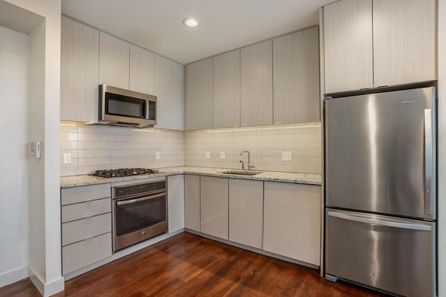 kitchen featuring sink, dark wood-type flooring, appliances with stainless steel finishes, tasteful backsplash, and light stone countertops