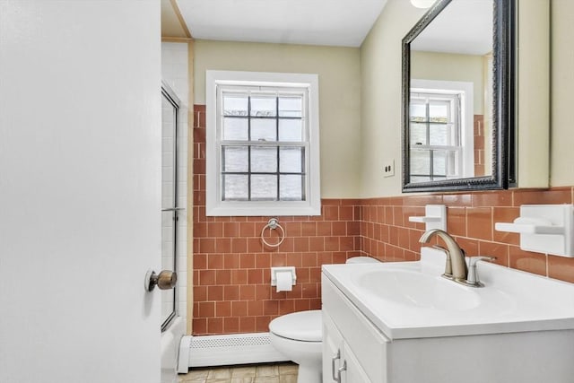 full bathroom with bath / shower combo with glass door, a baseboard radiator, tile walls, vanity, and toilet