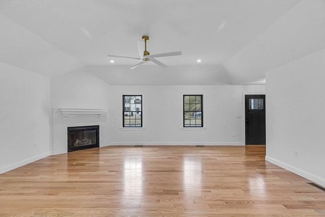 unfurnished living room with light wood finished floors, a glass covered fireplace, baseboards, and vaulted ceiling