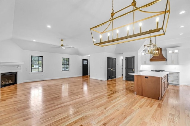 kitchen featuring a center island, premium range hood, open floor plan, ceiling fan with notable chandelier, and a fireplace