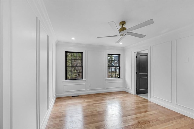 unfurnished bedroom featuring a ceiling fan, crown molding, a decorative wall, and light wood-style flooring