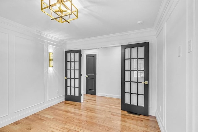 foyer entrance with crown molding, a decorative wall, light wood-style flooring, and a chandelier